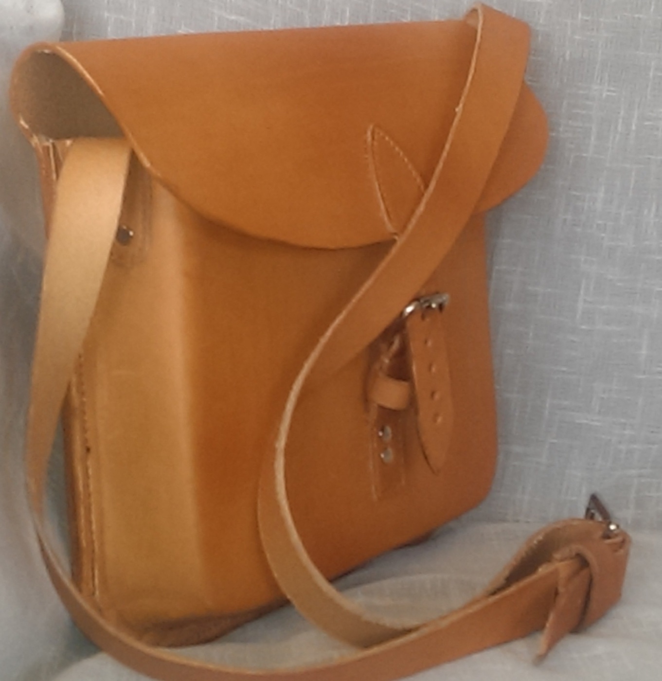 A handmade tan leather shoulder bag with a curved flap and long strap